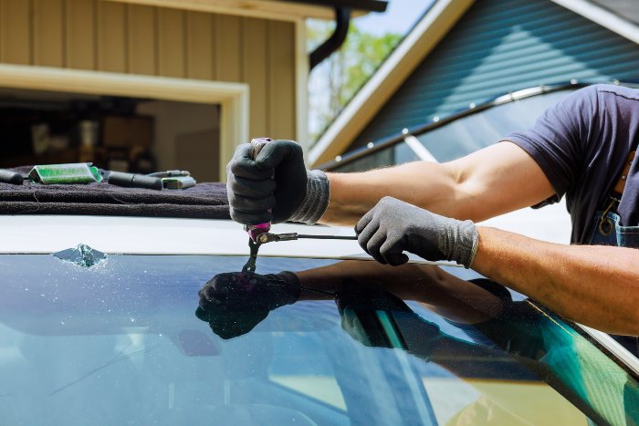 A man cleaning a car windshield with a tool, emphasizing the need for auto glass repair in Langley
