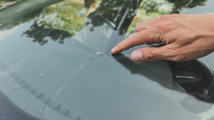 Person inspecting a car windshield, highlighting ICBC guidance for cracked glass in Langley, BC